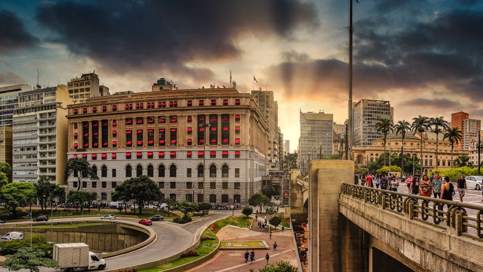 Picturesque view of old bridge above city road and house exteriors under bright cloudy sky in overcast weather at sundown in evening