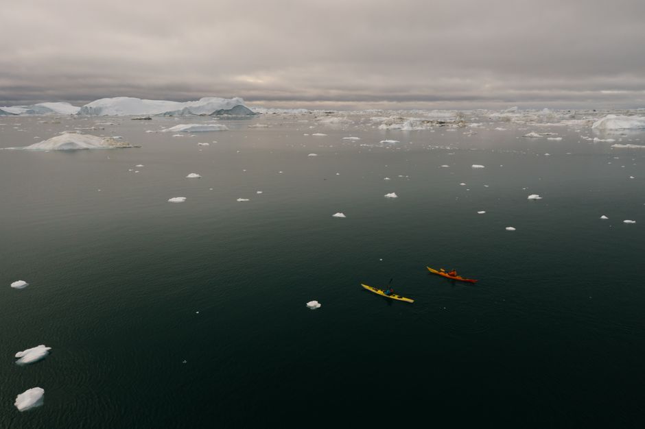 Two kayakers paddle through icy waters surrounded by floating icebergs.