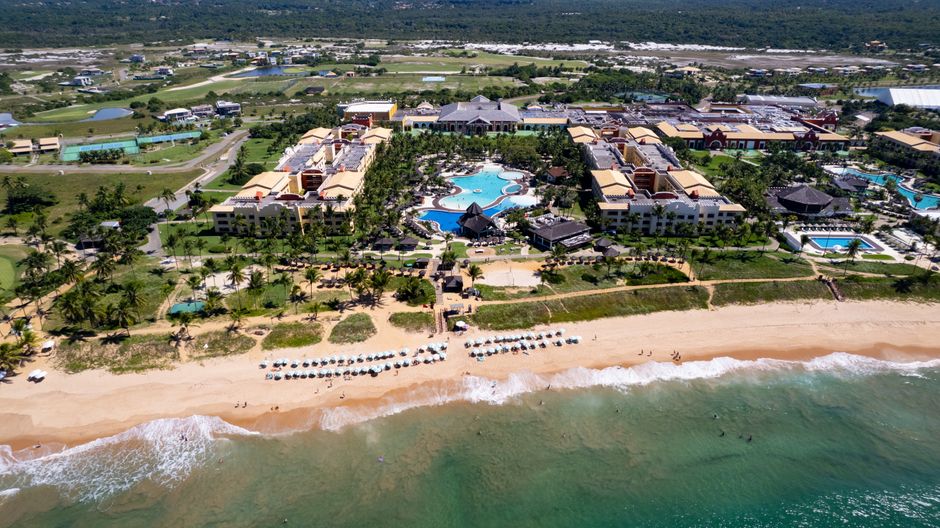 Aerial view of a luxury beachfront resort with expansive pool, villas, and sandy beach.